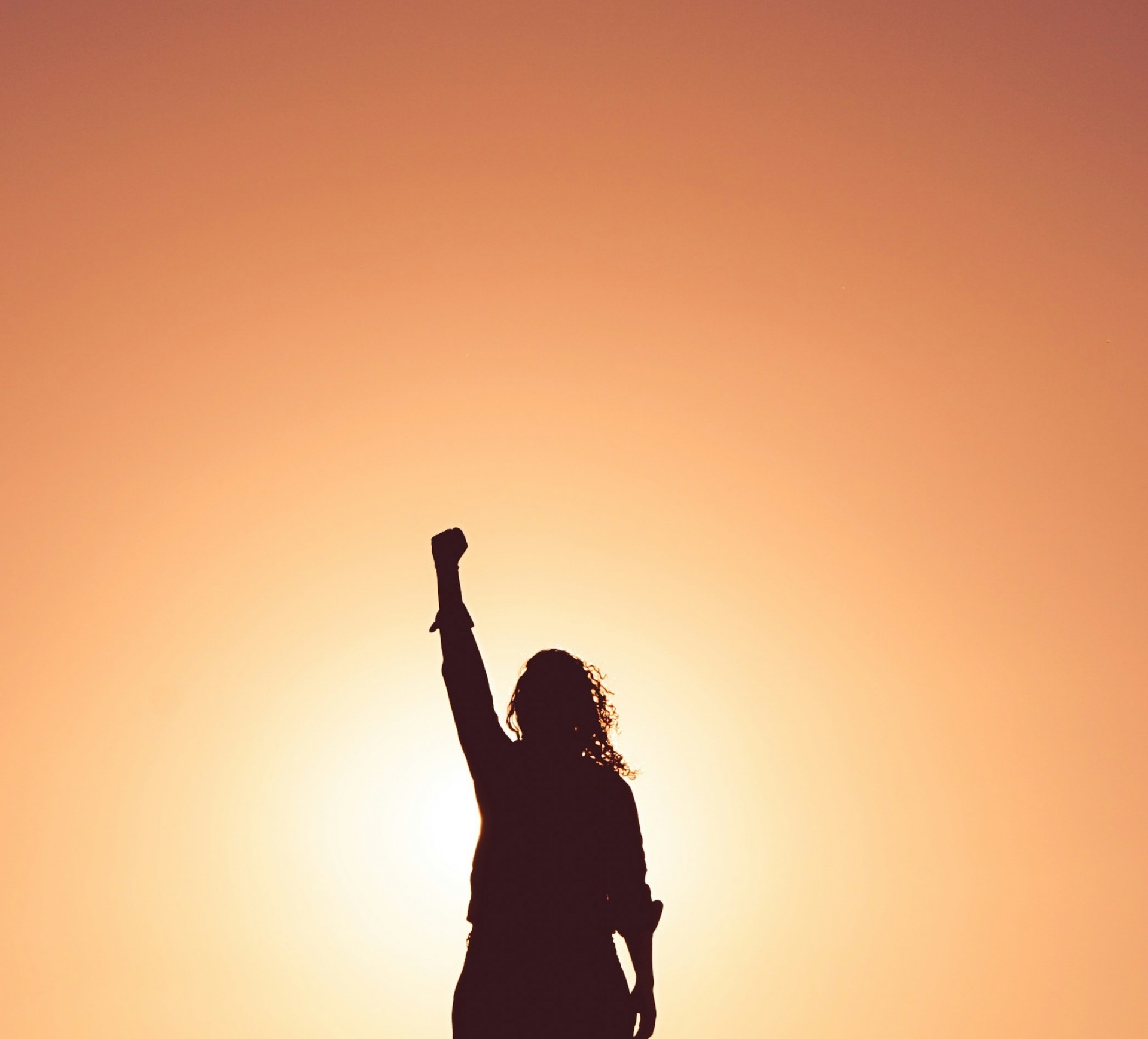 Woman raising her fist in triumph at sunset